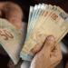 Pessoa segurando cédulas de R$ 50, representando o impacto positivo do reajuste do salário mínimo de 2026 na economia brasileira.