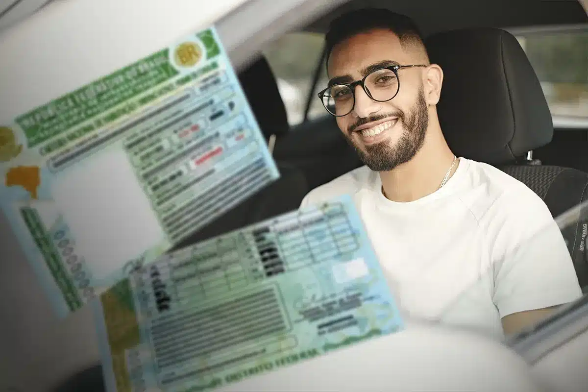 Jovem conduzindo e mostrando carteira de motorista brasileira Homem sorridente dentro do carro exibindo carteira de motorista brasileira.