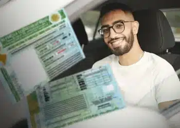 Homem de óculos sentado no banco do motorista segurando carteira nacional de habilitação