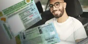 Homem de óculos sentado no banco do motorista segurando carteira nacional de habilitação