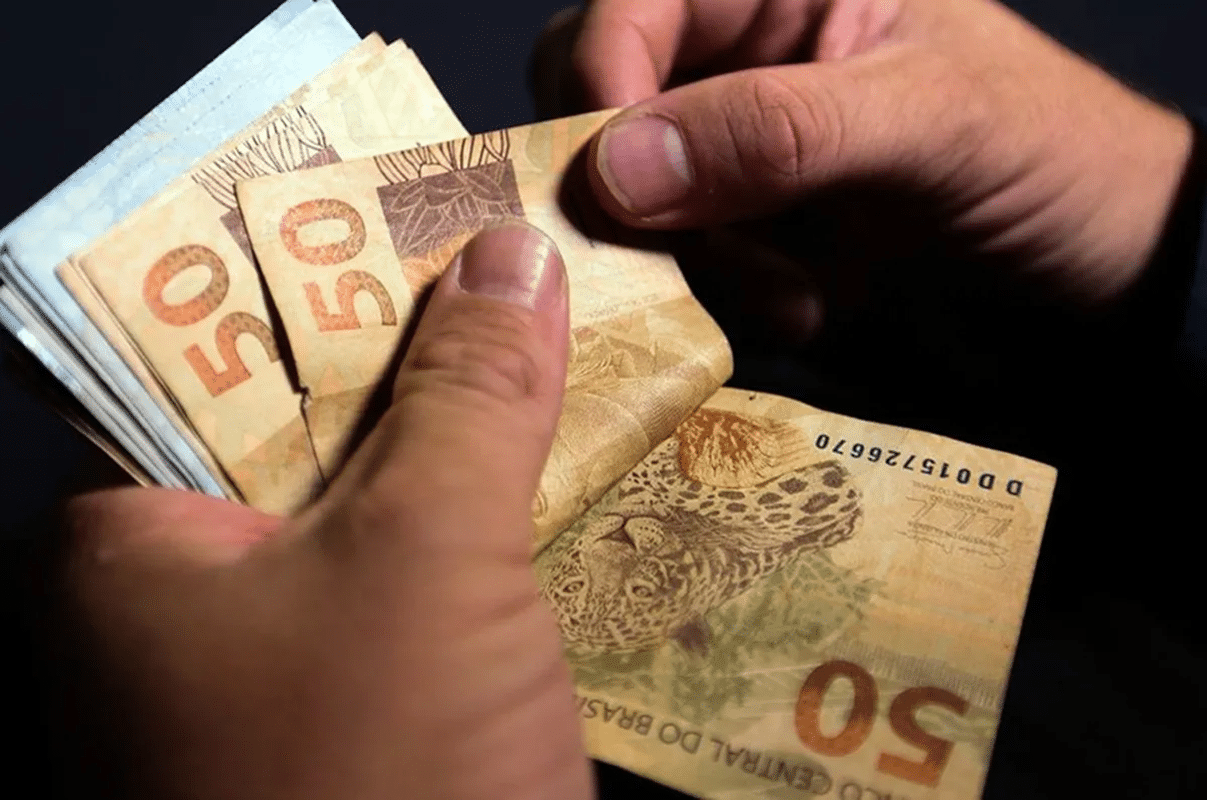 Mãos contando cédulas de 50 reais representando pagamento do Bolsa Família 2026