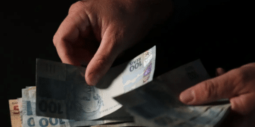 Mãos separando cédulas de 100 reais representando pagamento do Bolsa Família fevereiro 2026