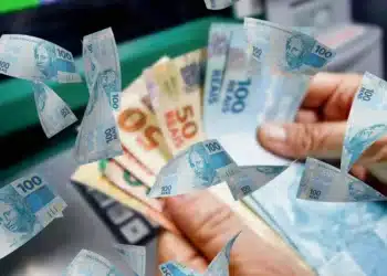 Notas de reais flutuando enquanto uma pessoa retira dinheiro do caixa eletrônico, representando o tema do salário mínimo em 2026.
