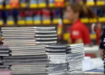 Pilha de vários cadernos espirais empilhados em loja, com pessoas desfocadas ao fundo