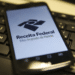 Smartphone exibindo o aplicativo da Receita Federal sobre teclado de computador