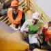 Profissionais de engenharia em canteiro de obras com equipamentos de segurança, revisando planos, refletindo sobre a NR-1 e a gestão de riscos psicossociais