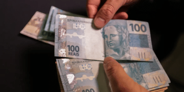 Mãos segurando diversas cédulas de 100 reais representando pagamento do INSS fevereiro 2026