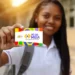 Jovem sorrindo exibe cartão colorido Pé-de-Meia na mão enquanto está na escola