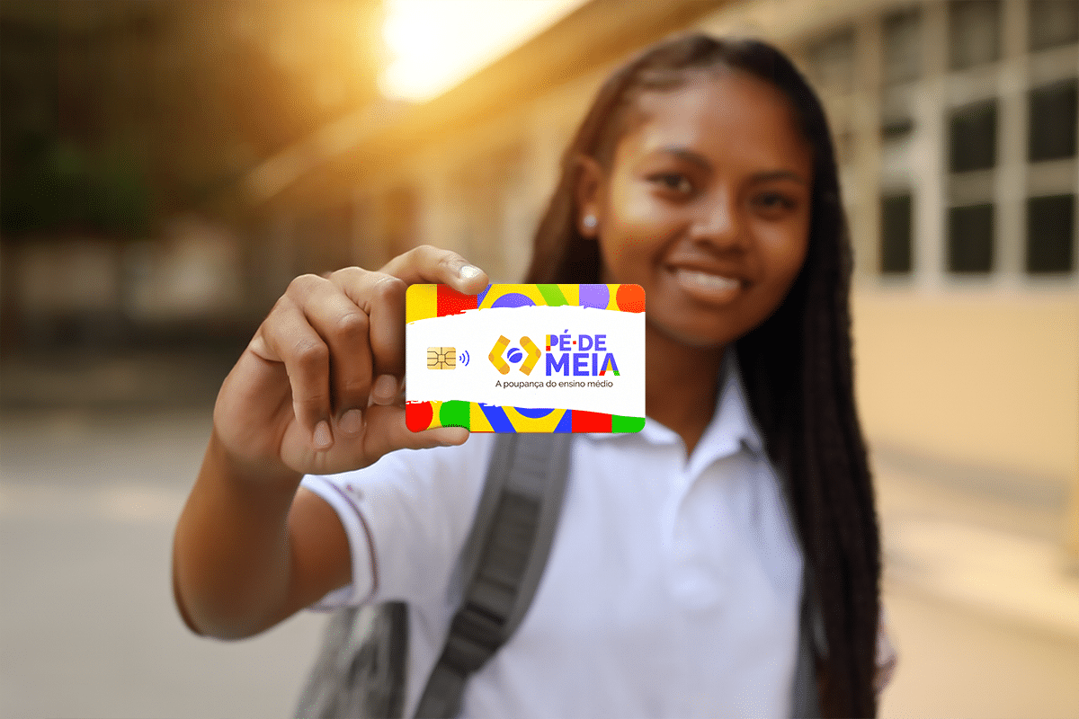 Beneficiária do Pé-de-Meia apresentando cartão do programa em frente a prédio escolar sob luz solar