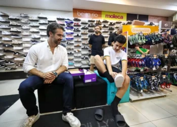 Governador Eduardo Leite acompanha o estudante Diogo Mendes na loja de calçados, enquanto ele escolhe o tênis para o uniforme, no contexto do programa 'Pé no Futuro 2026' que oferece R$150 para estudantes.