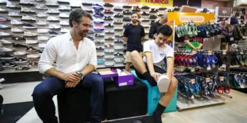 Governador Eduardo Leite acompanha o estudante Diogo Mendes na loja de calçados, enquanto ele escolhe o tênis para o uniforme, no contexto do programa 'Pé no Futuro 2026' que oferece R$150 para estudantes.