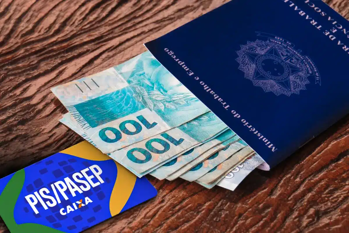 PIS/PASEP com carteira de trabalho e dinheiro Carteira de trabalho ao lado de dinheiro em notas de 100 reais e cartão PIS/PASEP Caixa