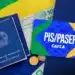 Imagem ilustrativa do PIS/PASEP, com o cartão da Caixa, cédulas de 100 reais, moedas e documentos relacionados, com fundo da bandeira do Brasil.