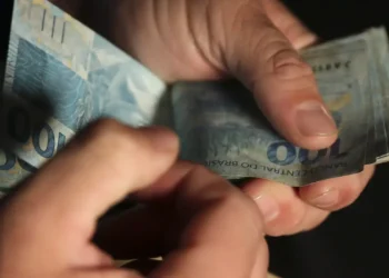 Mãos segurando e contando notas de 100 reais em fundo escuro de forma detalhada