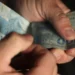 Mãos segurando e contando notas de 100 reais em fundo escuro de forma detalhada