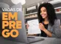 Mulher sorridente segurando contrato de trabalho em frente a laptop, simbolizando oportunidades de emprego com vagas no banco Bradesco.