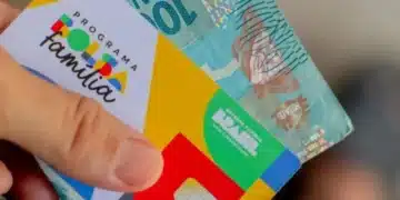 Cartão do Bolsa Família junto a cédula de dinheiro ilustrando renda familiar dentro do limite do programa.