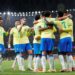 Jogadores da Seleção Brasileira de futebol, vestindo o uniforme oficial amarelo e azul, abraçados em comemoração no centro de um gramado de estádio iluminado à noite.