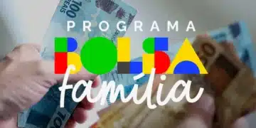 Mãos segurando cédulas de real com arte do programa Bolsa Família, indicando pagamento liberado em janeiro.
