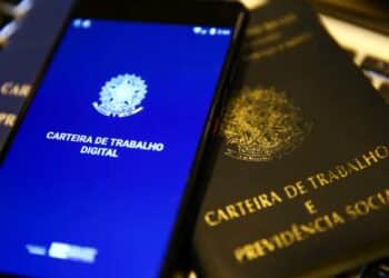 Tela do celular exibindo a Carteira de Trabalho Digital ao lado da versão física, simbolizando a digitalização dos registros profissionais.