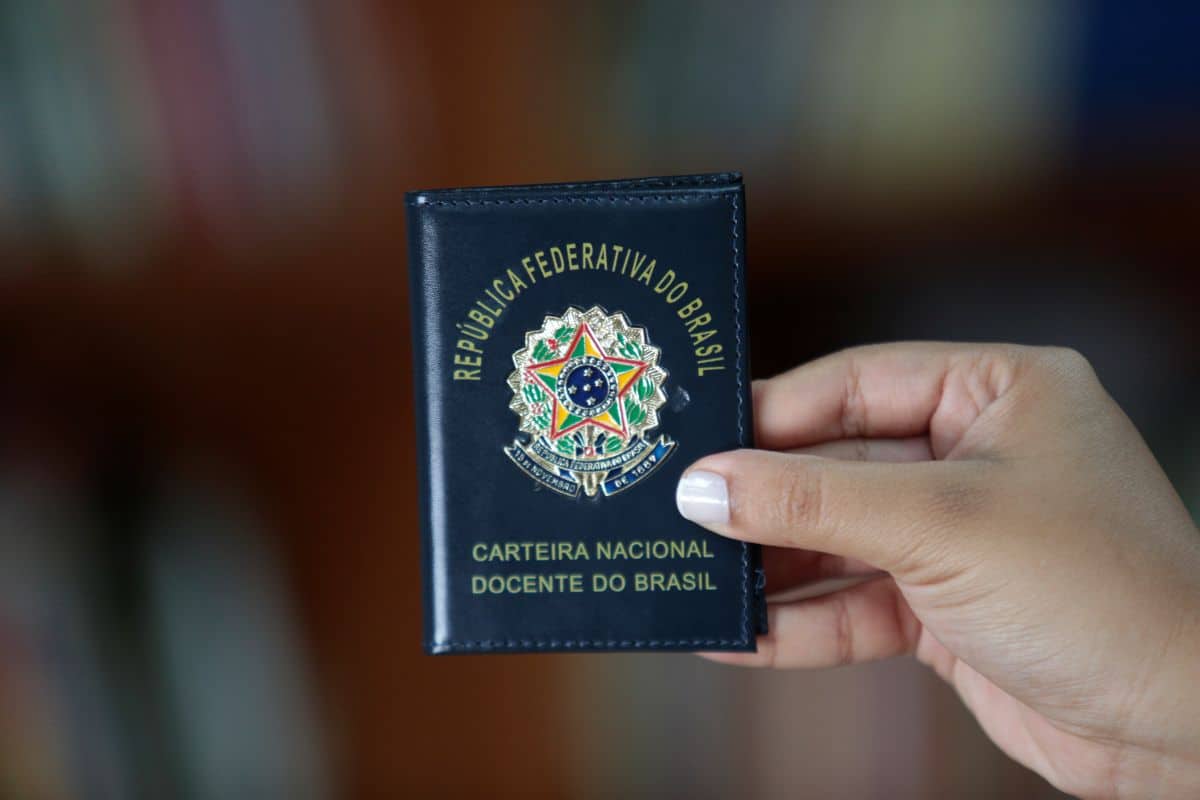 Mão segurando carteira nacional do docente do Brasil com brasão e texto em destaque