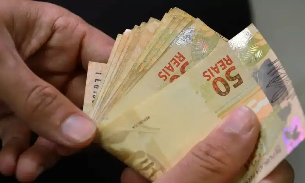 Valores a Receber: como consultar e resgatar dinheiro de pessoas falecidas. Notas de cinquenta reais em mãos, representando valores a receber de pessoa falecida.