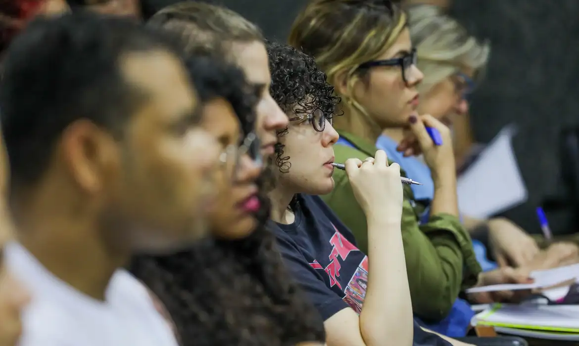 Pessoas atentas em conferência ou aula Grupo de pessoas sentadas, prestando atenção em palestra ou reunião, algumas anotando e outras pensativas