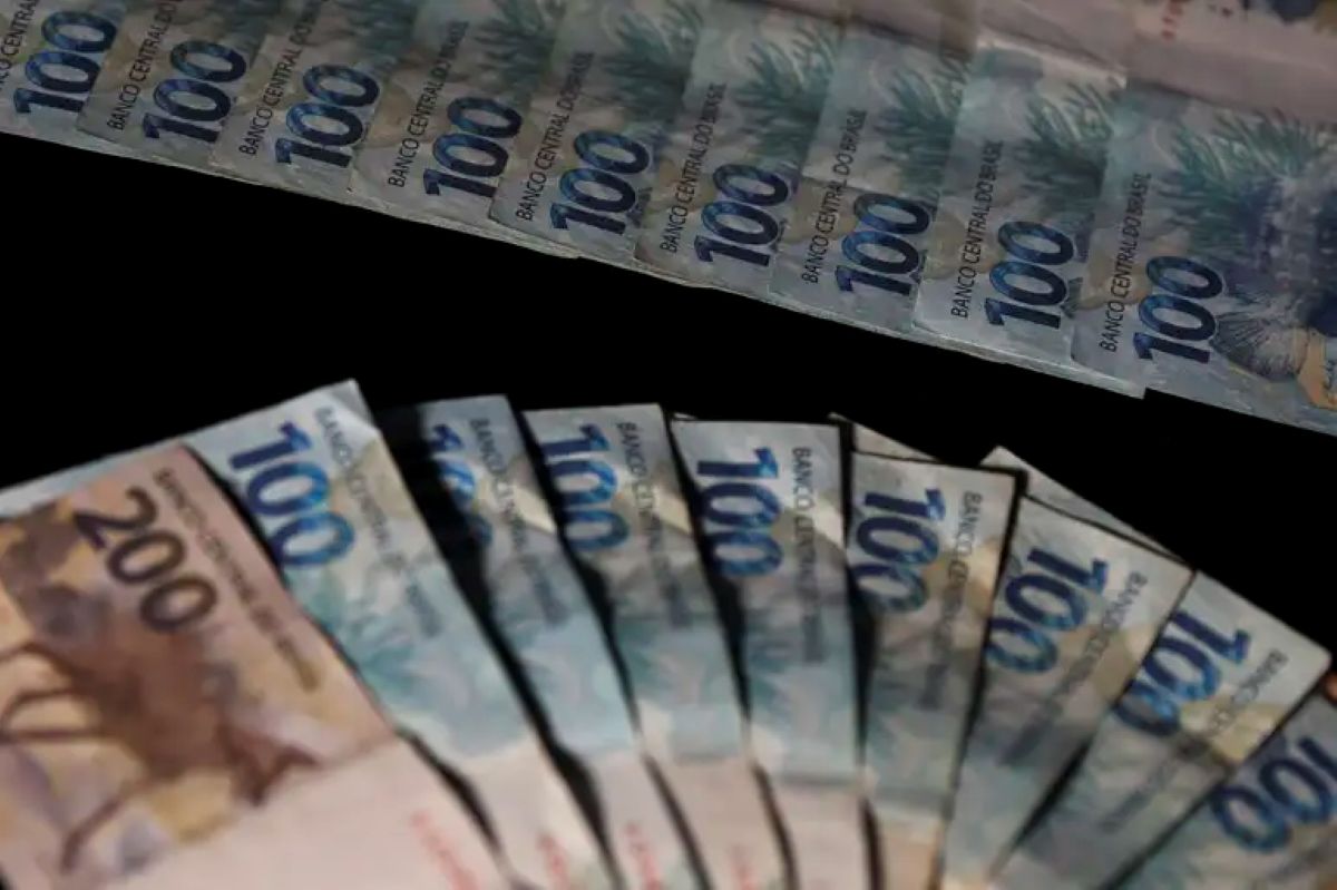 Várias cédulas de dinheiro brasileiro em valores de 100 e 200 reais sobre fundo preto