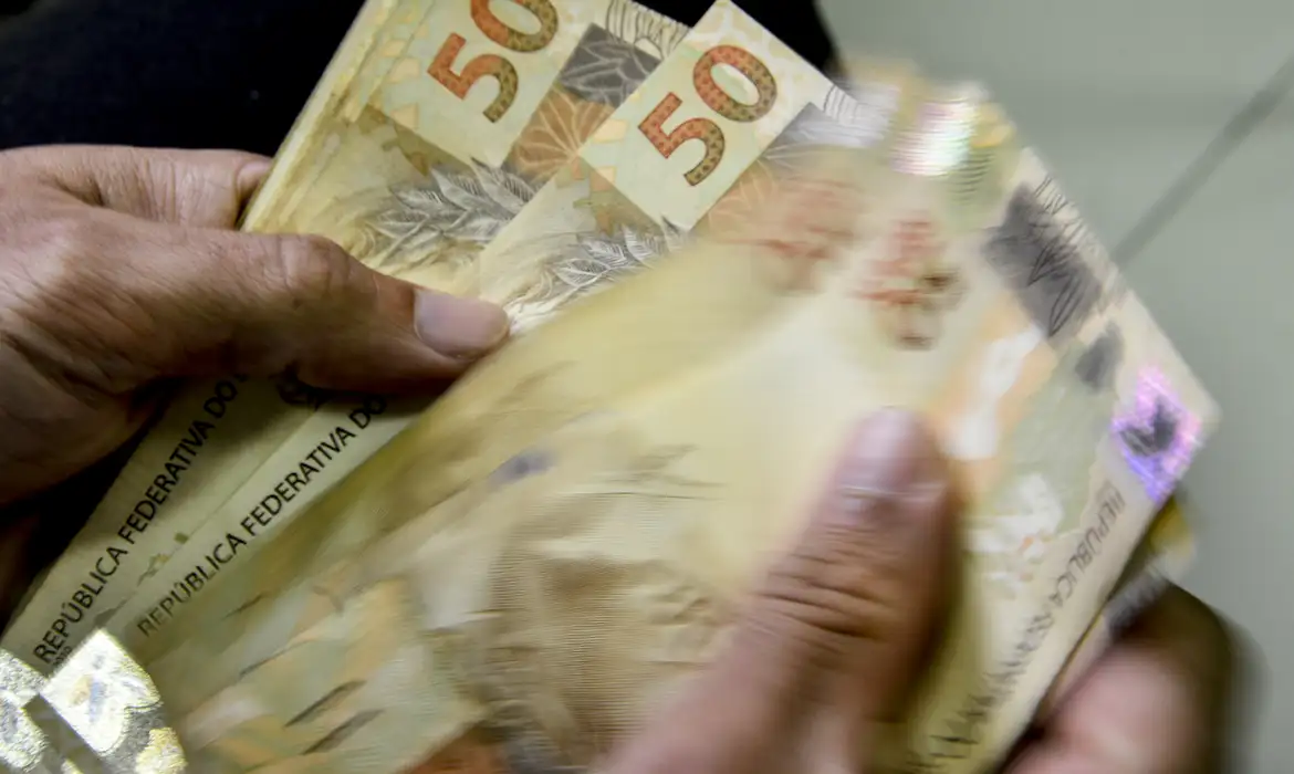 Mãos Contando Dinheiro em Reais Brasileiros Duas mãos masculinas contando cédulas de 50 reais brasileiras em movimento desfocado
