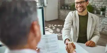 Homem em entrevista de emprego apertando as mãos com o entrevistador, enquanto apresenta seu currículo.