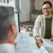 Homem em entrevista de emprego apertando as mãos com o entrevistador, enquanto apresenta seu currículo.