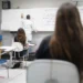 Professor escrevendo fórmulas químicas no quadro branco em sala com estudantes atentos sentados