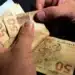 Mãos de trabalhador contando notas de cinquenta reais referentes ao abono salarial.