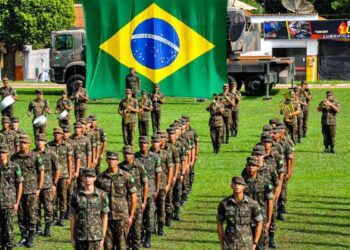 Jovens realizando o alistamento militar com a bandeira do Brasil ao fundo.