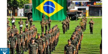 Jovens realizando o alistamento militar com a bandeira do Brasil ao fundo.