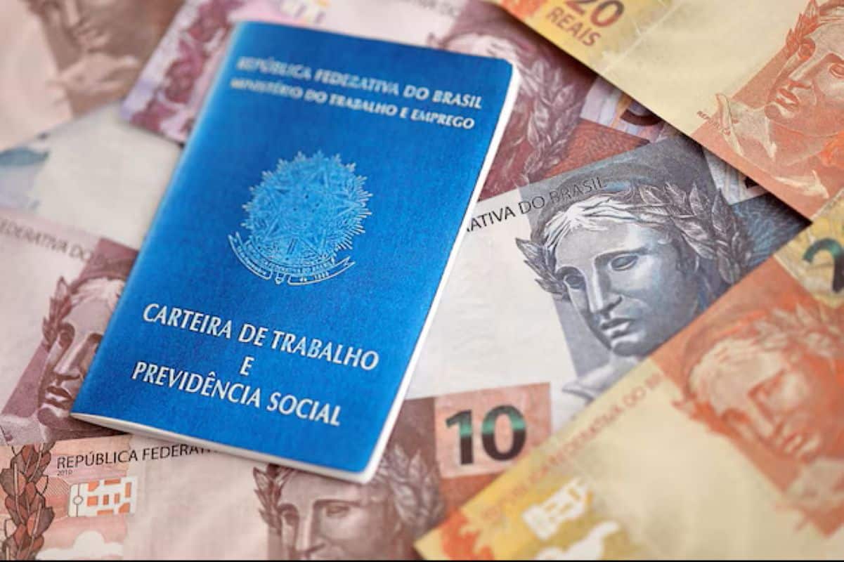 Carteira de Trabalho e cédulas de dinheiro ilustrando o impacto do reajuste do salário mínimo no Seguro-Desemprego em 2026.