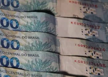 Cédulas de 100 reais do Brasil empilhadas, com detalhes visíveis das cores e elementos de segurança.