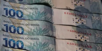 Cédulas de 100 reais do Brasil empilhadas, com detalhes visíveis das cores e elementos de segurança.