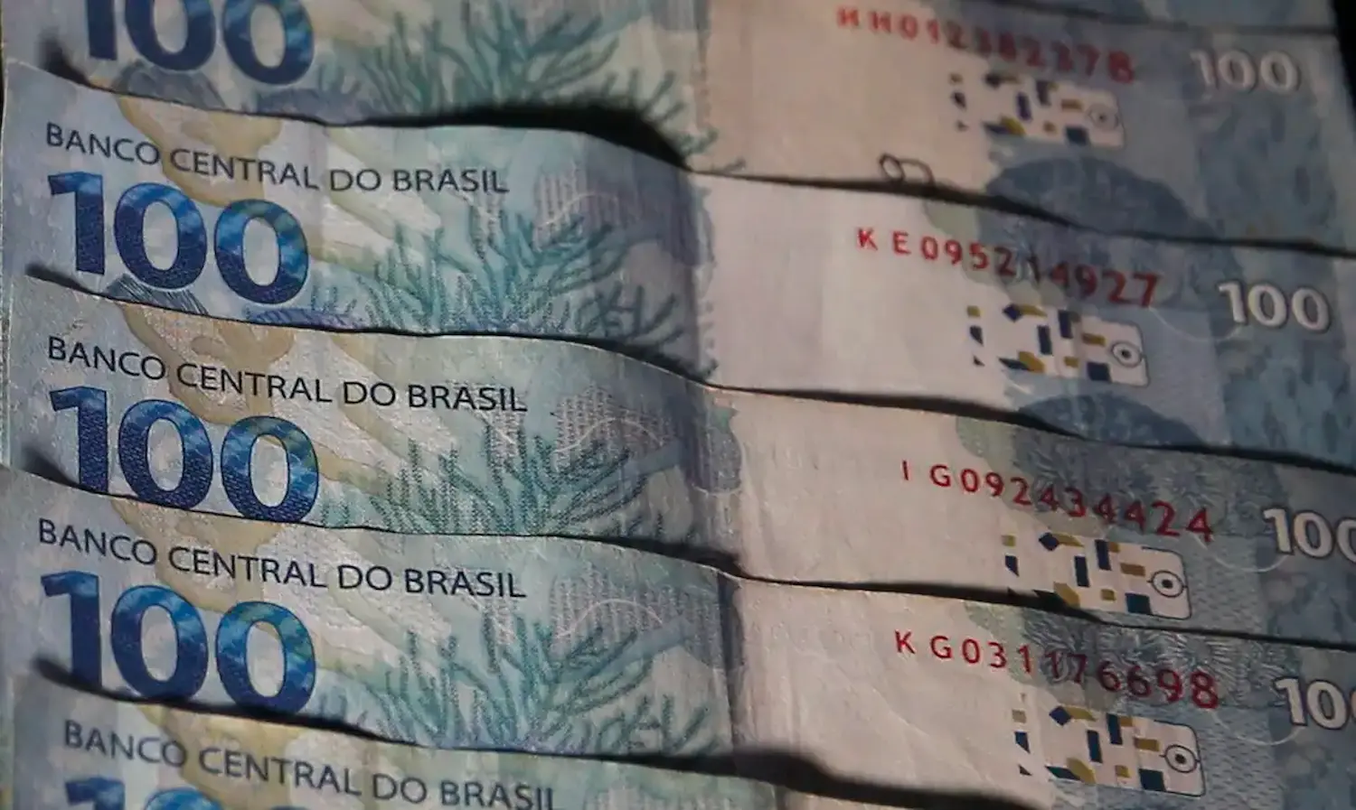 Reajustes do INSS Cédulas de 100 reais do Brasil empilhadas, com detalhes visíveis das cores e elementos de segurança.