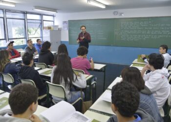 Professor de inglês dá aula para turma de adolescentes em sala de aula com estudantes atentos.