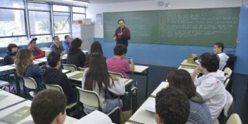 Professor de inglês dá aula para turma de adolescentes em sala de aula com estudantes atentos.