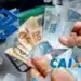 Mãos segurando cédulas de real, com os logotipos do Banco do Brasil e da Caixa Econômica Federal, representando o pagamento do Abono Salarial