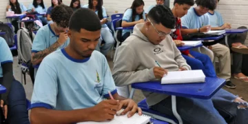 Alunos em sala de aula escrevendo em cadernos, foco no ensino em 2026
