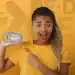 Jovem sorrindo e apontando para a tela de um celular com o logo do Pé-de-Meia, que oferece apoio a estudantes.