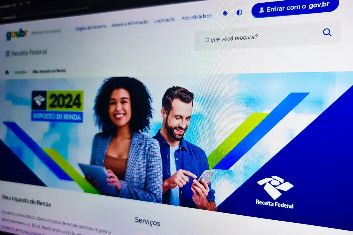 quem tem direito isenção irpf 2026 limite 5 mil Tela de um monitor exibindo o portal oficial gov.br da Receita Federal. No centro, um banner com um homem e uma mulher sorrindo e segurando dispositivos eletrônicos, ao lado do logotipo da Receita Federal e a inscrição "Imposto de Renda".