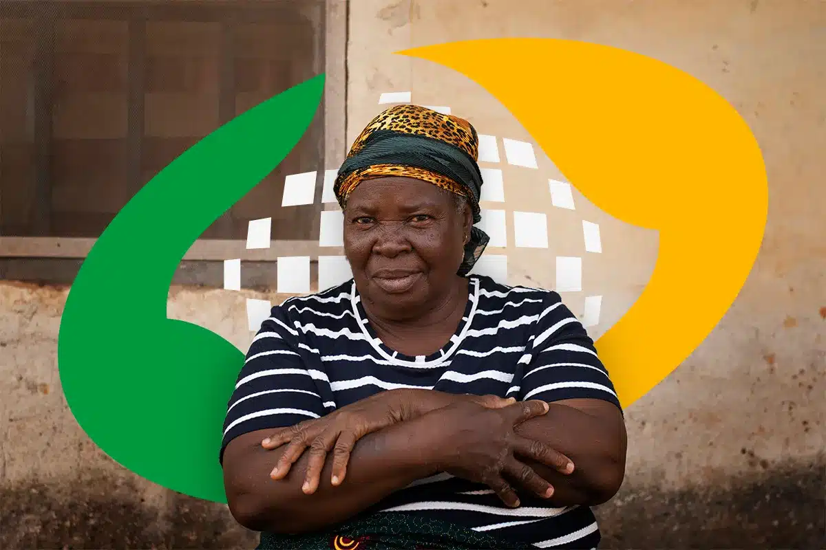 contribuintes desconto inss obrigatorio 2026. Mulher negra idosa com turbante estampado e blusa listrada, de braços cruzados, sorrindo em frente a uma parede rústica, com o logotipo da Previdência Social (ícone verde e amarelo) sobreposto ao fundo.