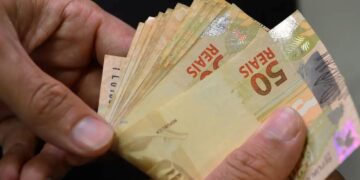 Pessoa segurando cédulas de R$50, ilustrando o reajuste do salário mínimo para 2026 e os pagamentos do INSS.