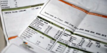 Close em duas faturas de energia elétrica impressas em papel branco, com detalhes em verde e laranja. O foco está nos campos de "Composição da Tarifa", "Impostos" e "Indicadores de Continuidade", mostrando os valores e taxas detalhados.