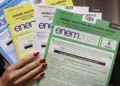 Mão feminina segura cadernos coloridos do Enem 2025, nas cores azul, amarelo, branco e verde.