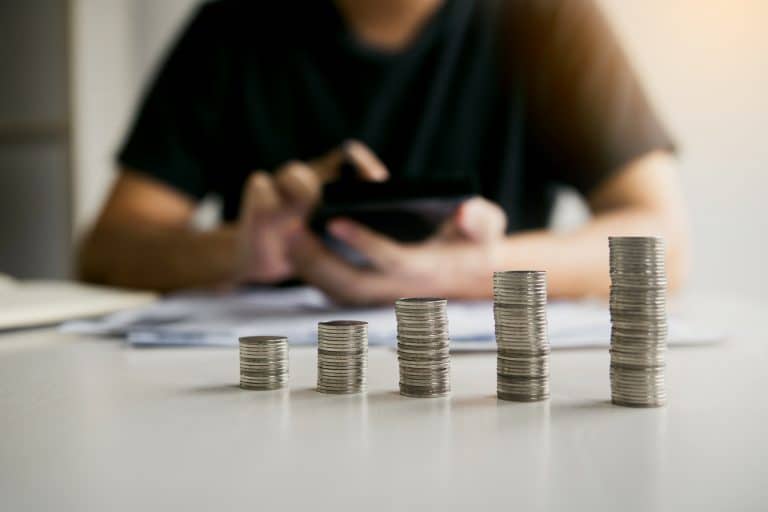 Empilhamento de moedas representando diferentes faixas salariais no Brasil em 2026, com o fundo desfocado e um celular em mãos.